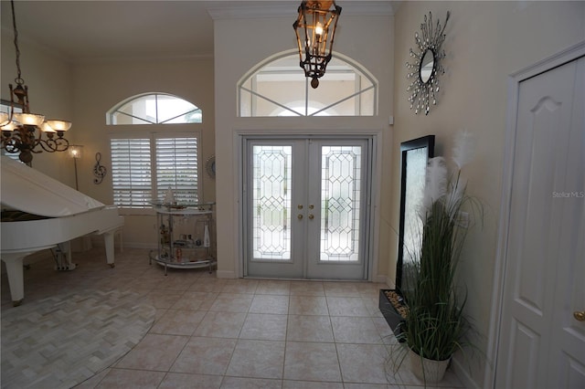 tiled foyer entrance with a chandelier, ornamental molding, a wealth of natural light, and french doors