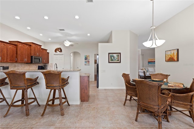 kitchen with light stone countertops, ceiling fan, a kitchen breakfast bar, pendant lighting, and decorative backsplash