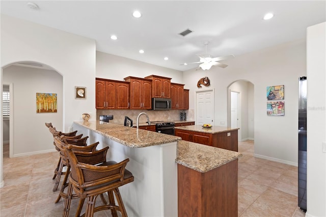 kitchen with ceiling fan, tasteful backsplash, kitchen peninsula, a kitchen island, and appliances with stainless steel finishes