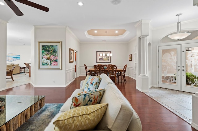 living room with french doors, ceiling fan with notable chandelier, ornamental molding, dark hardwood / wood-style flooring, and decorative columns