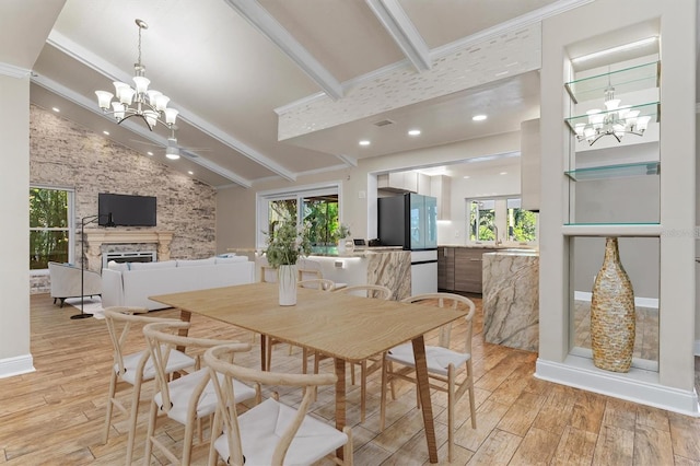 dining space featuring lofted ceiling with beams, a healthy amount of sunlight, a stone fireplace, and light hardwood / wood-style flooring