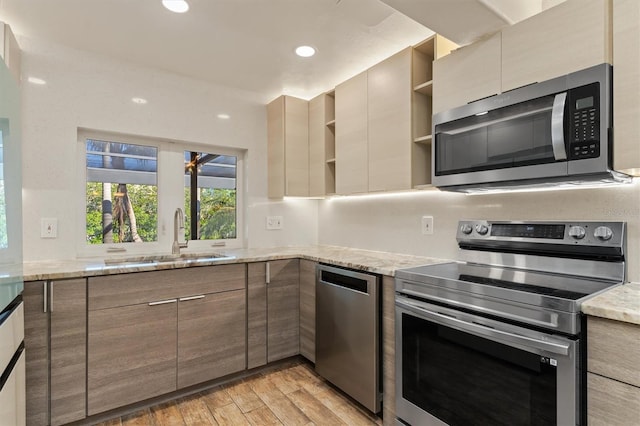 kitchen featuring light stone countertops, light wood-type flooring, sink, and appliances with stainless steel finishes