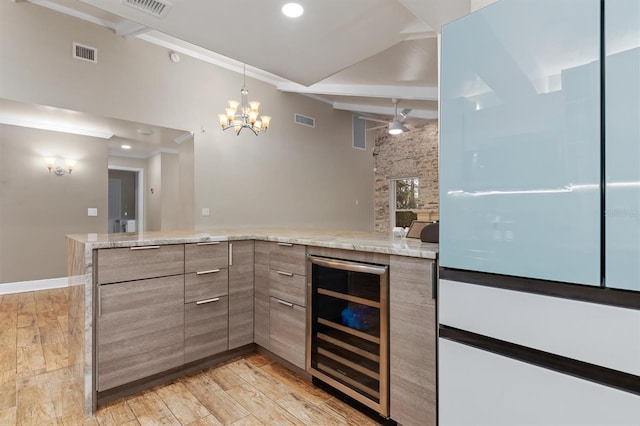 kitchen with light stone countertops, ceiling fan with notable chandelier, beverage cooler, crown molding, and light hardwood / wood-style floors