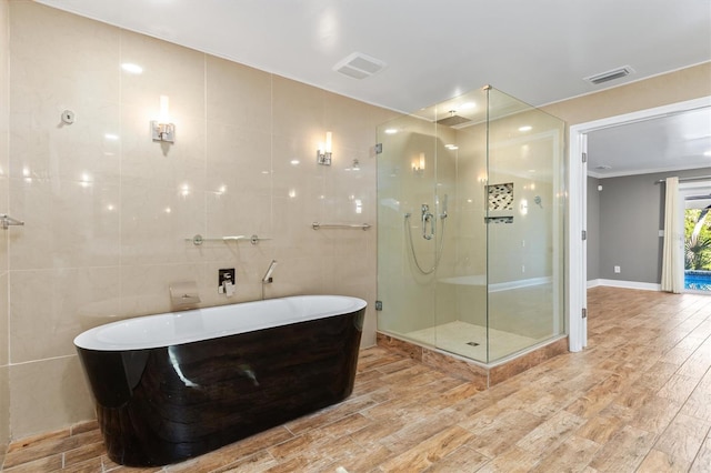 bathroom with wood-type flooring, ornamental molding, tile walls, and independent shower and bath