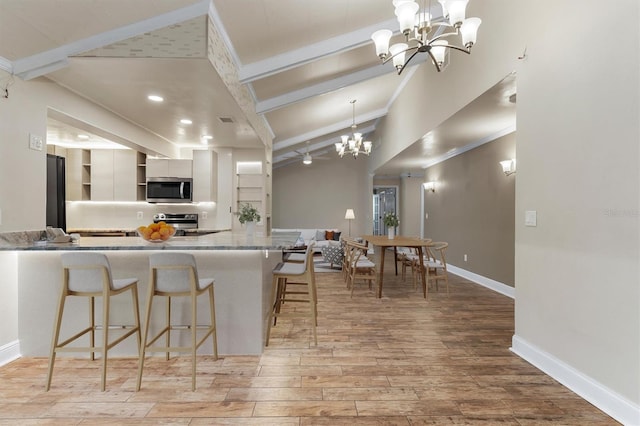 kitchen featuring a breakfast bar, white cabinets, light hardwood / wood-style flooring, vaulted ceiling with beams, and appliances with stainless steel finishes