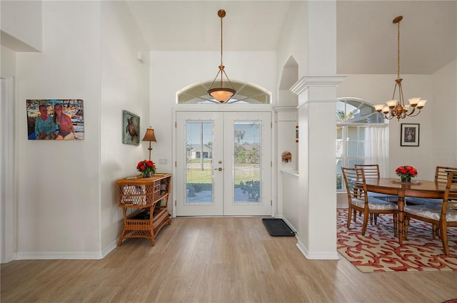 entryway with a notable chandelier, ornate columns, light wood-type flooring, and french doors