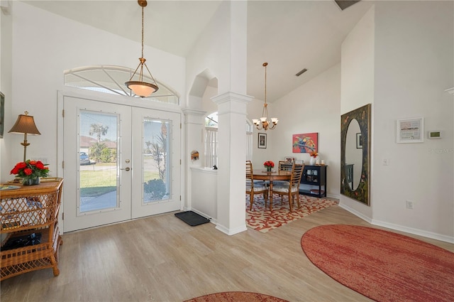 entrance foyer with high vaulted ceiling, french doors, ornate columns, light wood-type flooring, and a notable chandelier