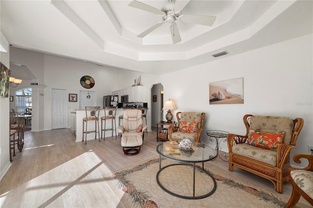 living room featuring a tray ceiling, ceiling fan, and light hardwood / wood-style floors