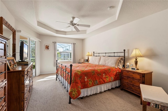 bedroom with light carpet, a textured ceiling, a tray ceiling, and ceiling fan