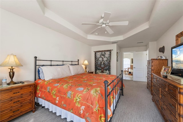 bedroom with a raised ceiling, ceiling fan, and light colored carpet