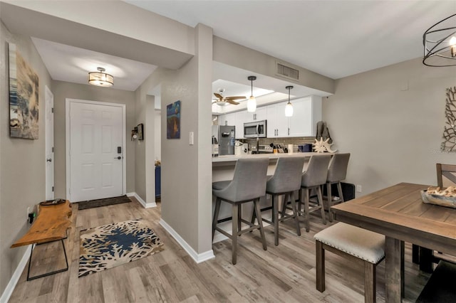 kitchen with kitchen peninsula, appliances with stainless steel finishes, backsplash, white cabinets, and hanging light fixtures