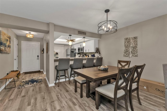 dining space with a raised ceiling, light hardwood / wood-style flooring, and a notable chandelier