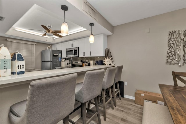 kitchen featuring white cabinets, a raised ceiling, a breakfast bar area, and appliances with stainless steel finishes