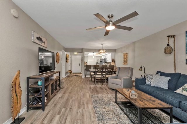 living room featuring ceiling fan with notable chandelier, light wood-style floors, and baseboards