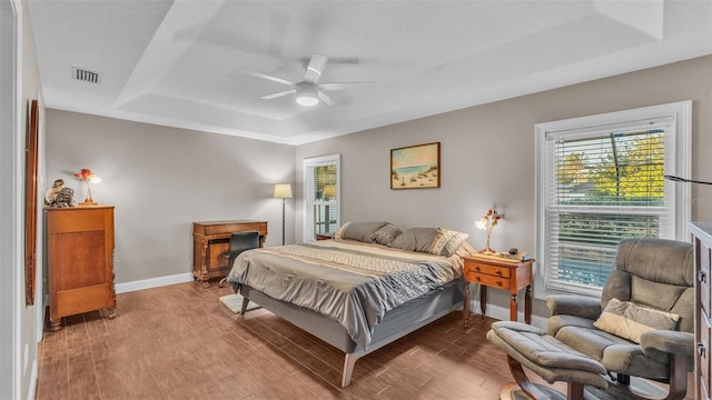 bedroom with wood-type flooring, a tray ceiling, and ceiling fan