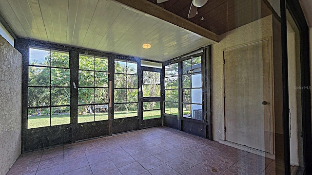 unfurnished sunroom featuring beamed ceiling and ceiling fan