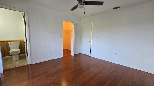 unfurnished bedroom featuring ensuite bathroom, a walk in closet, dark hardwood / wood-style floors, ceiling fan, and a closet