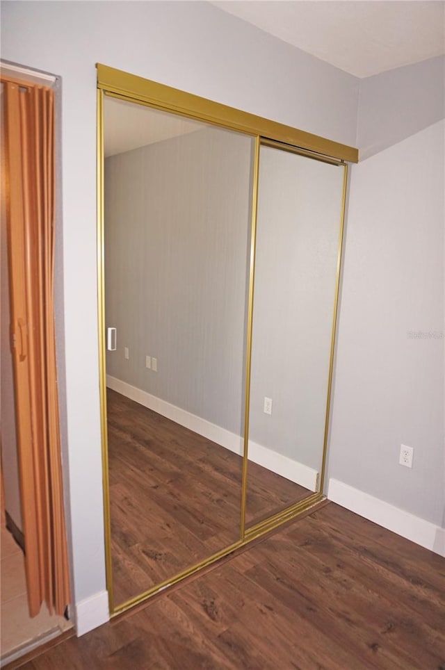 unfurnished bedroom featuring a closet, wood finished floors, and baseboards