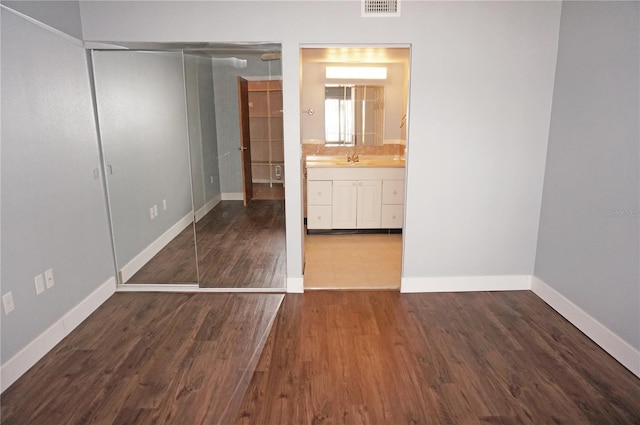 unfurnished bedroom featuring visible vents, baseboards, connected bathroom, wood finished floors, and a closet