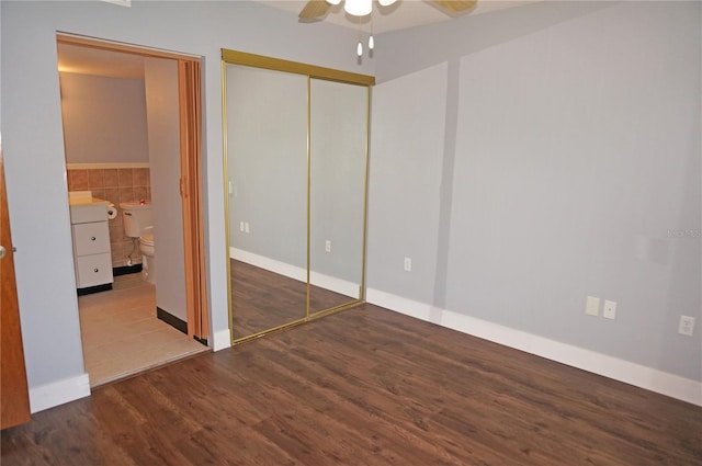 unfurnished bedroom featuring tile walls, a closet, ceiling fan, ensuite bath, and wood finished floors