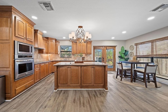 kitchen with a center island, stainless steel appliances, light hardwood / wood-style flooring, a chandelier, and custom exhaust hood