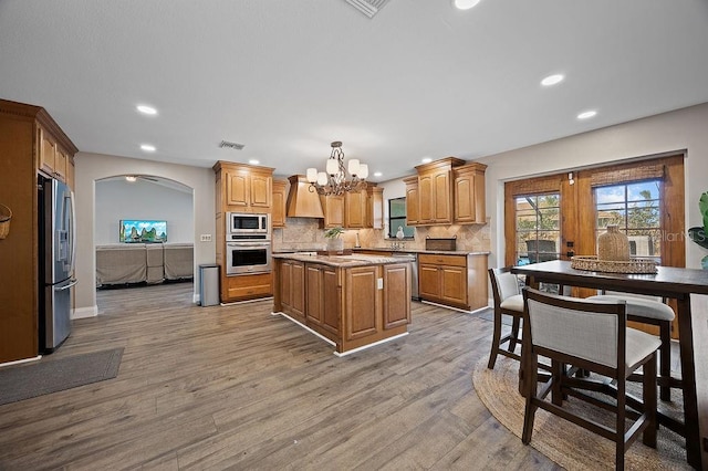 kitchen with light wood-type flooring, appliances with stainless steel finishes, a center island, and decorative light fixtures