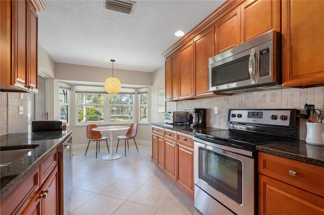 kitchen with decorative backsplash, dark stone counters, decorative light fixtures, and appliances with stainless steel finishes