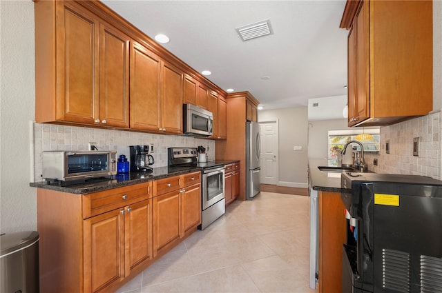 kitchen with dark stone countertops, sink, light tile patterned floors, and appliances with stainless steel finishes