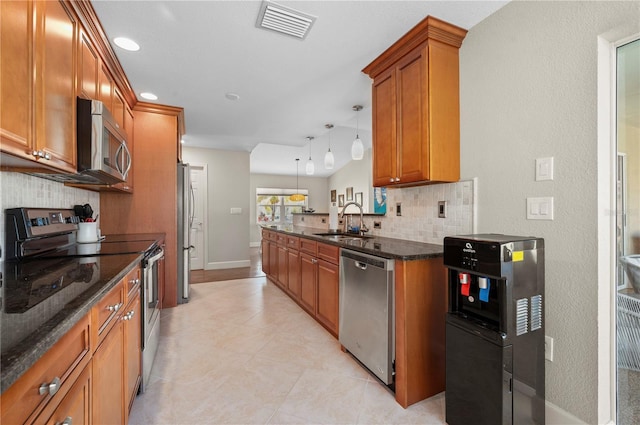 kitchen with appliances with stainless steel finishes, backsplash, sink, pendant lighting, and dark stone countertops