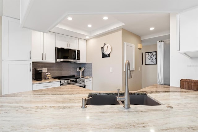 kitchen with sink, a raised ceiling, light stone counters, white cabinets, and appliances with stainless steel finishes