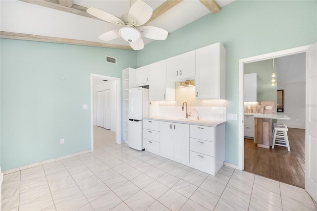 kitchen featuring backsplash, ceiling fan, beamed ceiling, white fridge, and white cabinetry