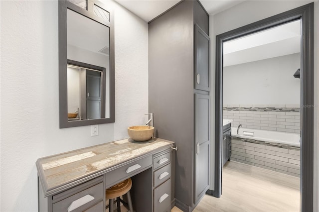 bathroom featuring wood-type flooring, vanity, and a relaxing tiled tub