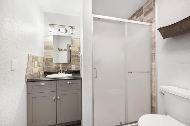 bathroom featuring backsplash, vanity, a shower with shower door, and toilet