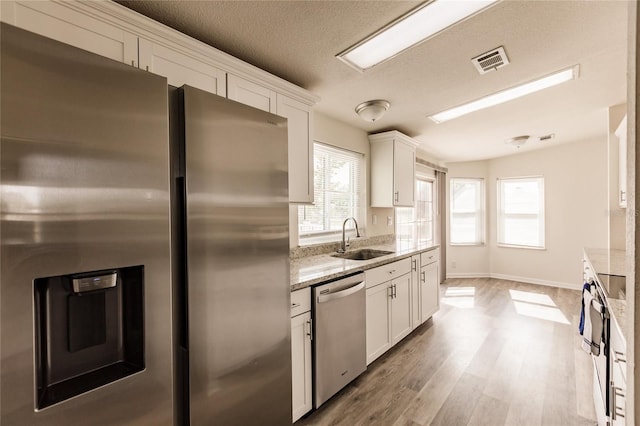 kitchen with light stone countertops, white cabinetry, sink, and appliances with stainless steel finishes