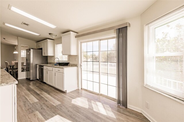 kitchen with stainless steel dishwasher, white cabinets, light stone countertops, and light hardwood / wood-style flooring