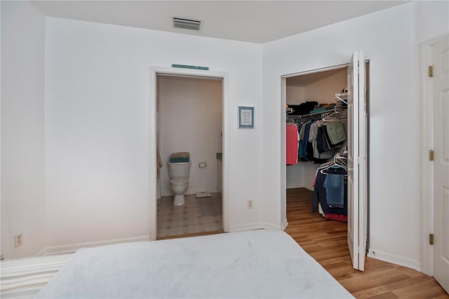 bedroom featuring a walk in closet, light hardwood / wood-style flooring, a closet, and connected bathroom