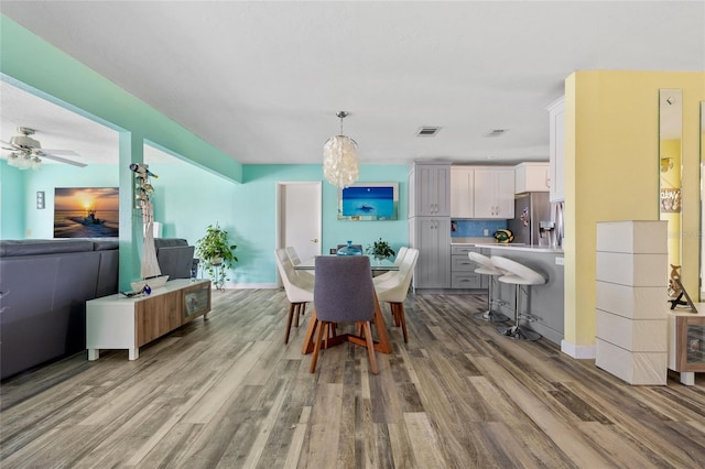 dining space with ceiling fan with notable chandelier and light hardwood / wood-style floors