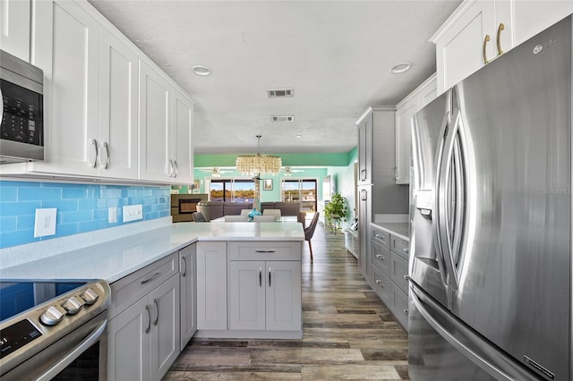 kitchen featuring hanging light fixtures, stainless steel appliances, dark hardwood / wood-style floors, kitchen peninsula, and a chandelier