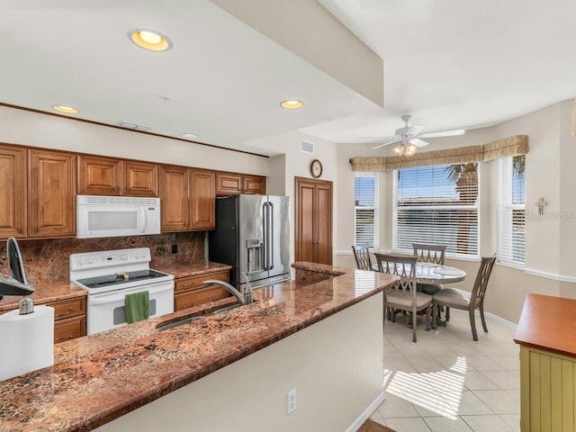 kitchen featuring white appliances, backsplash, sink, dark stone countertops, and light tile patterned floors