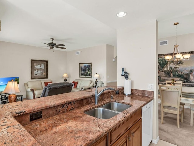 kitchen with stone counters, white dishwasher, ceiling fan with notable chandelier, hanging light fixtures, and sink