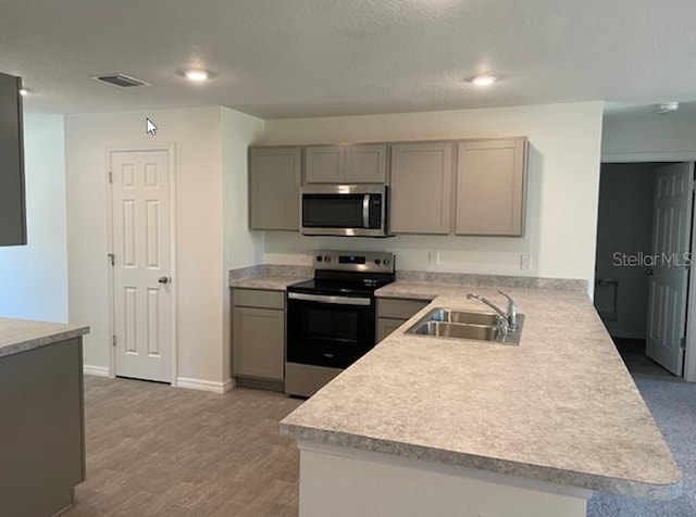 kitchen featuring sink, gray cabinets, light wood-type flooring, kitchen peninsula, and stainless steel appliances