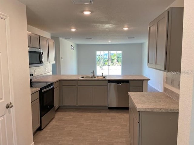 kitchen featuring kitchen peninsula, sink, gray cabinets, and appliances with stainless steel finishes