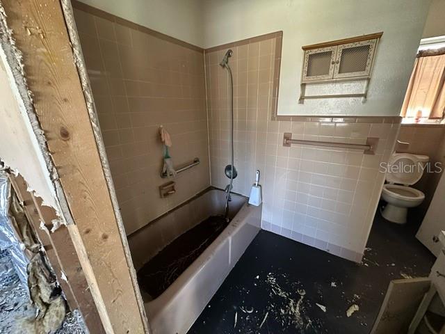 bathroom with tiled shower / bath combo, toilet, and tile walls