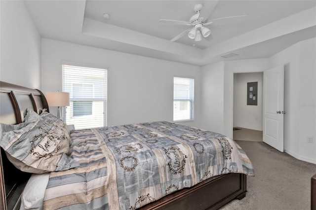 carpeted bedroom featuring ceiling fan, a raised ceiling, and multiple windows