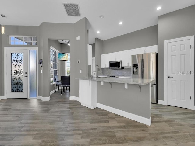 kitchen with white cabinetry, ceiling fan, light hardwood / wood-style flooring, kitchen peninsula, and a kitchen bar