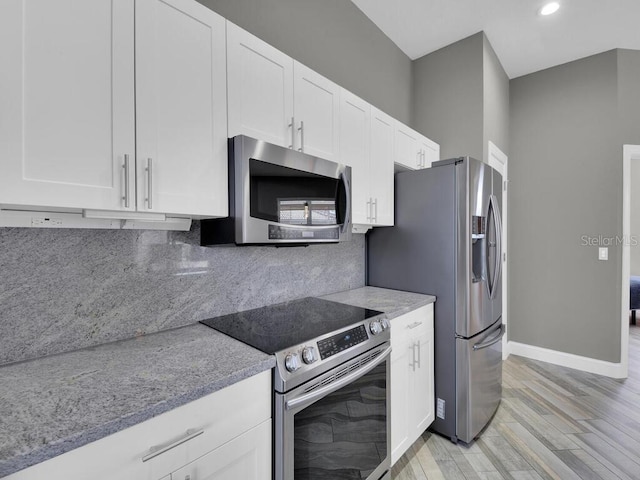 kitchen with white cabinets, decorative backsplash, stainless steel appliances, and light hardwood / wood-style floors