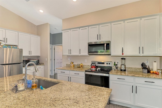 kitchen with light stone countertops, stainless steel appliances, sink, white cabinetry, and lofted ceiling