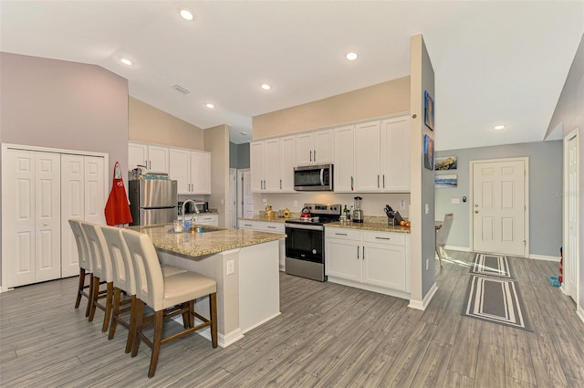 kitchen featuring light stone counters, white cabinetry, stainless steel appliances, and an island with sink