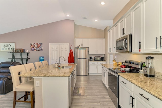 kitchen with white cabinetry, stainless steel appliances, light hardwood / wood-style floors, lofted ceiling, and a kitchen island with sink