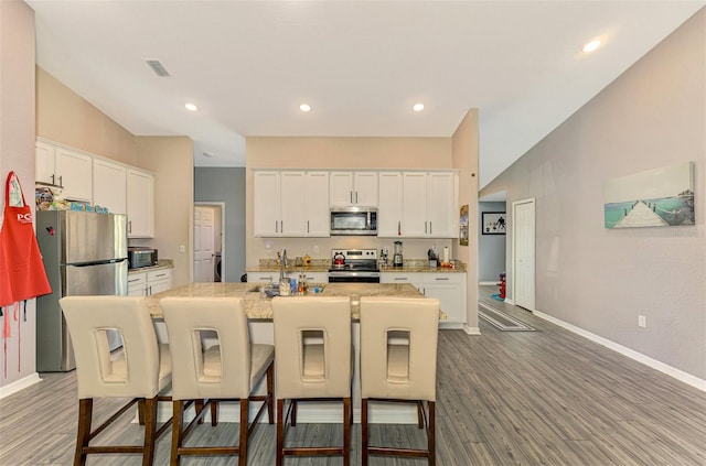 kitchen with hardwood / wood-style floors, white cabinetry, an island with sink, and appliances with stainless steel finishes